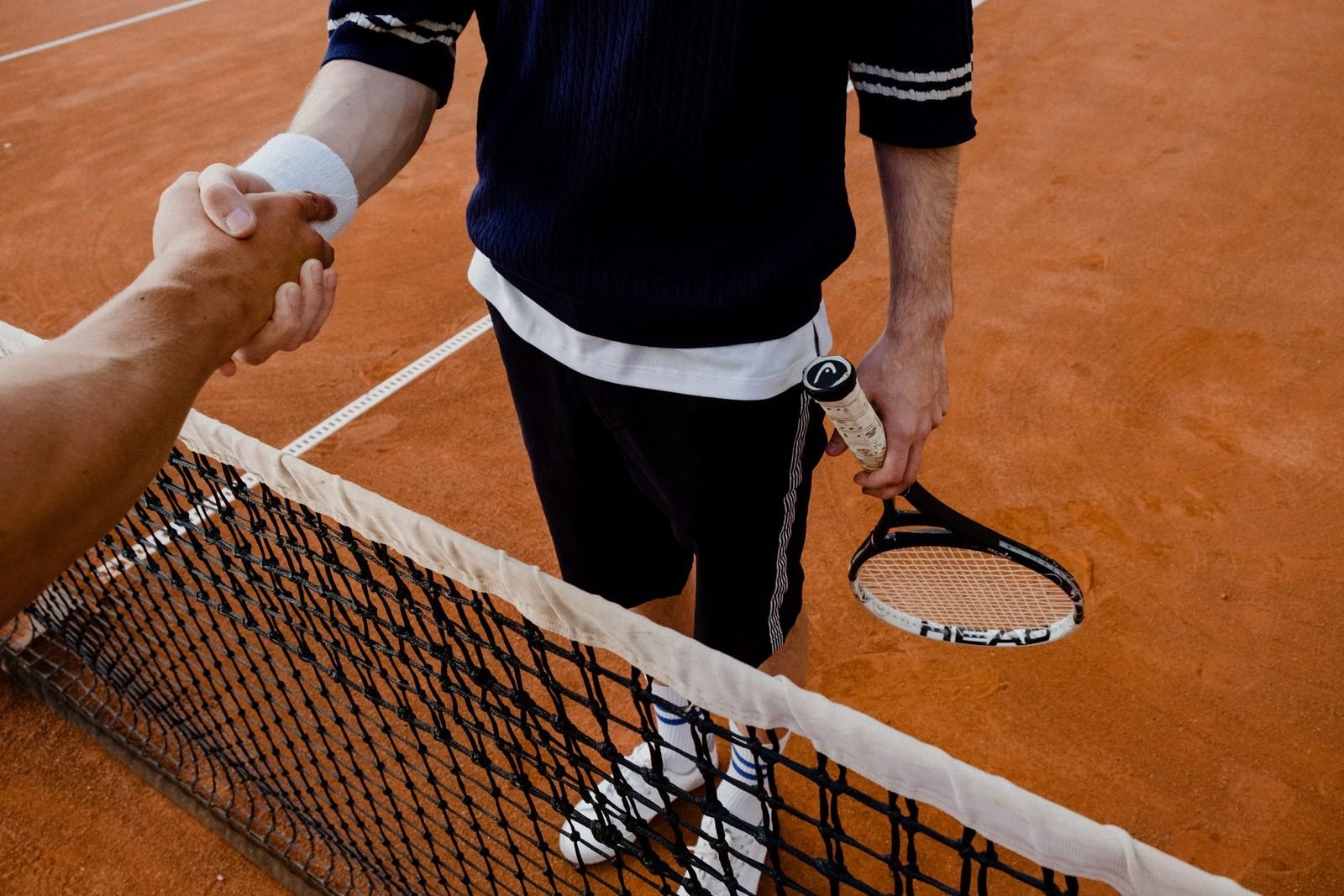 Tennis player at the net reaching for a handshake — symbolising connection on and off the court